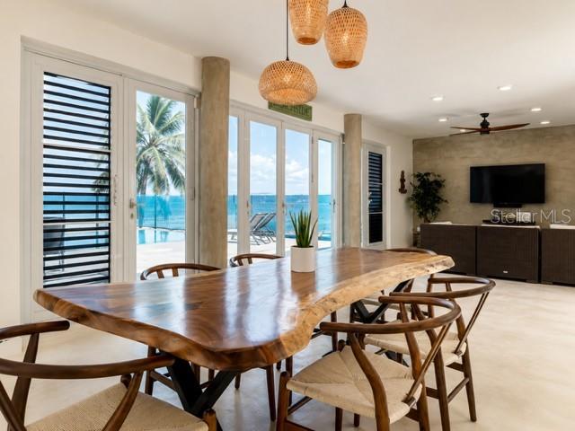 A dining room features a live-edge wooden table, woven chairs, and sliding glass doors overlooking the ocean — 14 CAMINO LAS PICUAS, RIO GRANDE, PR