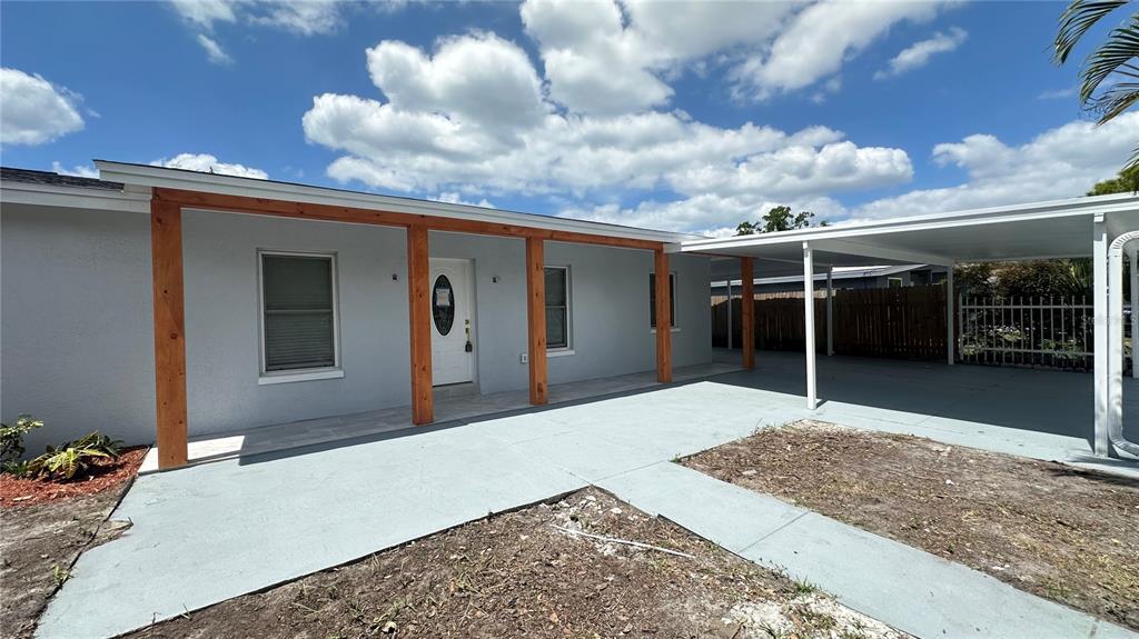 A single-story house exterior features a covered front porch with wood posts and a carport — 6405 S MANHATTAN AVENUE, TAMPA, FL