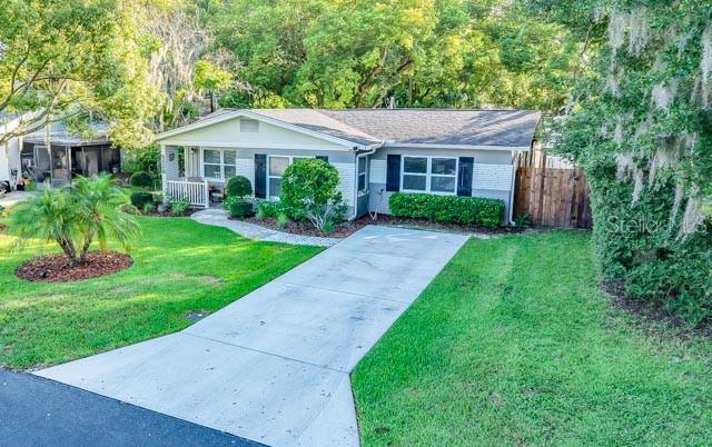 A covered front porch features a brick floor, white railings, two wicker chairs, and a door — 5725 14TH STREET, ZEPHYRHILLS, FL