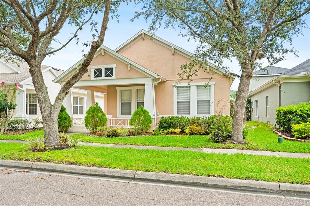 A single-story peach-colored house with a front porch and two large trees in the yard — 14475 JAMAICA DOGWOOD DRIVE, ORLANDO, FL