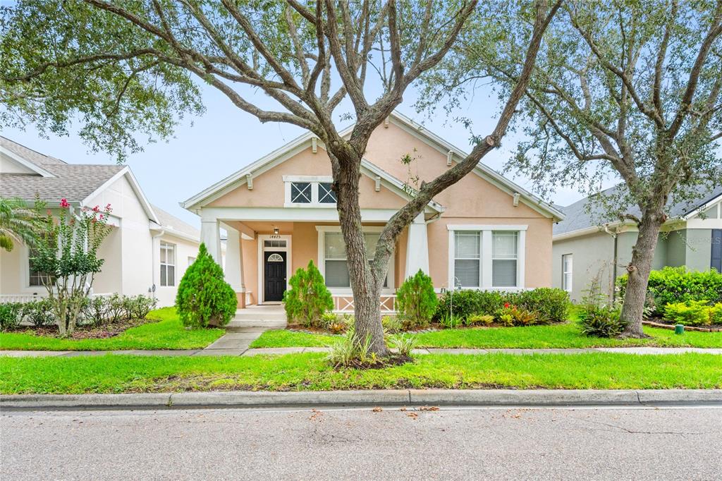 A single-story peach-colored house with a front porch and a large tree in the yard — 14475 JAMAICA DOGWOOD DRIVE, ORLANDO, FL