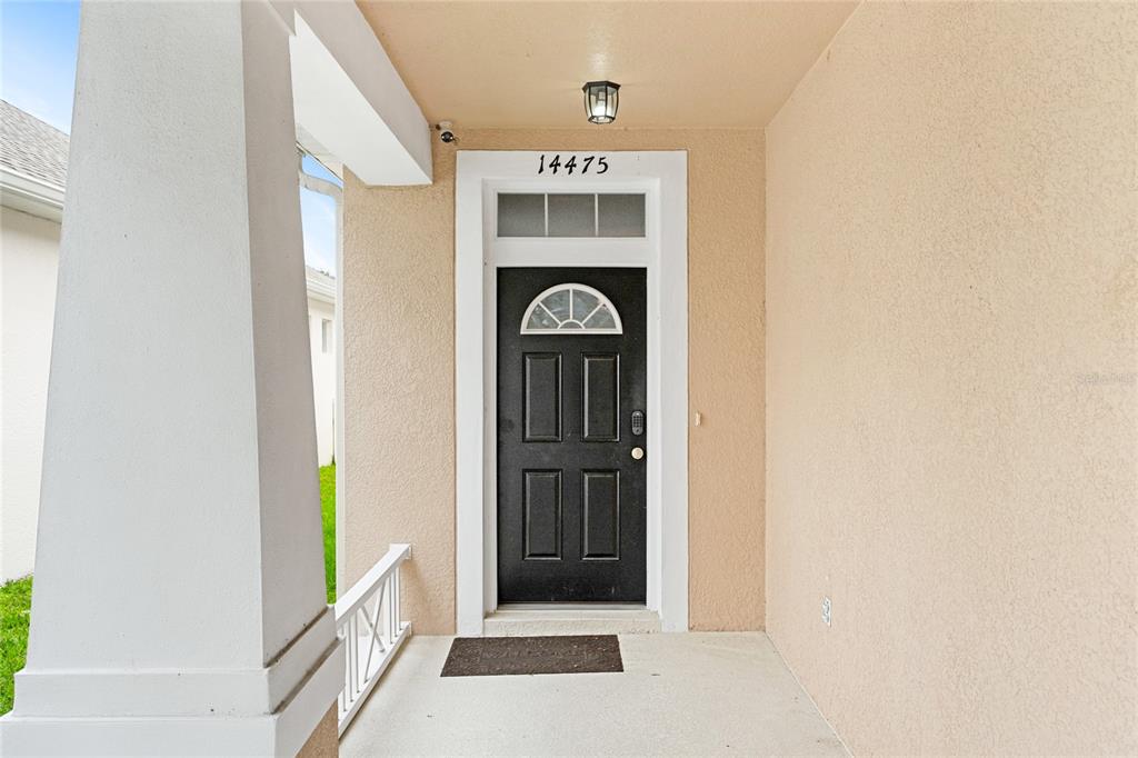 A black front door with a transom window sits under a covered porch — 14475 JAMAICA DOGWOOD DRIVE, ORLANDO, FL