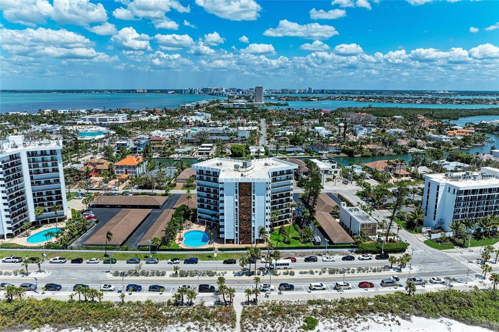 An aerial view shows multi-story residential buildings, swimming pools, and parking lots near the coast — 101 BENJAMIN FRANKLIN DRIVE UNIT 46, SARASOTA, FL