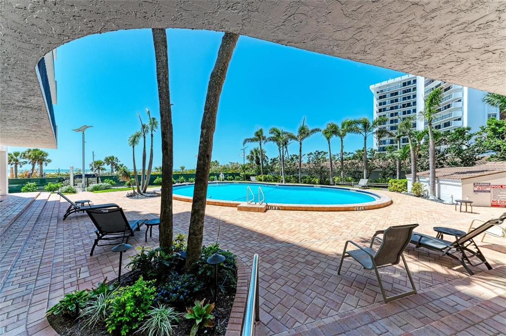 A swimming pool sits on a brick patio surrounded by palm trees and lounge chairs — 101 BENJAMIN FRANKLIN DRIVE UNIT 46, SARASOTA, FL