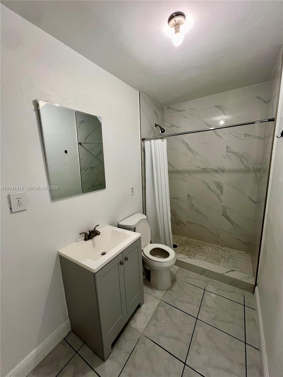 A bathroom features a gray vanity, a toilet, and a tiled walk-in shower — 5410 W 7th Ave # 1, Hialeah FL 33012, HIALEAH, FL