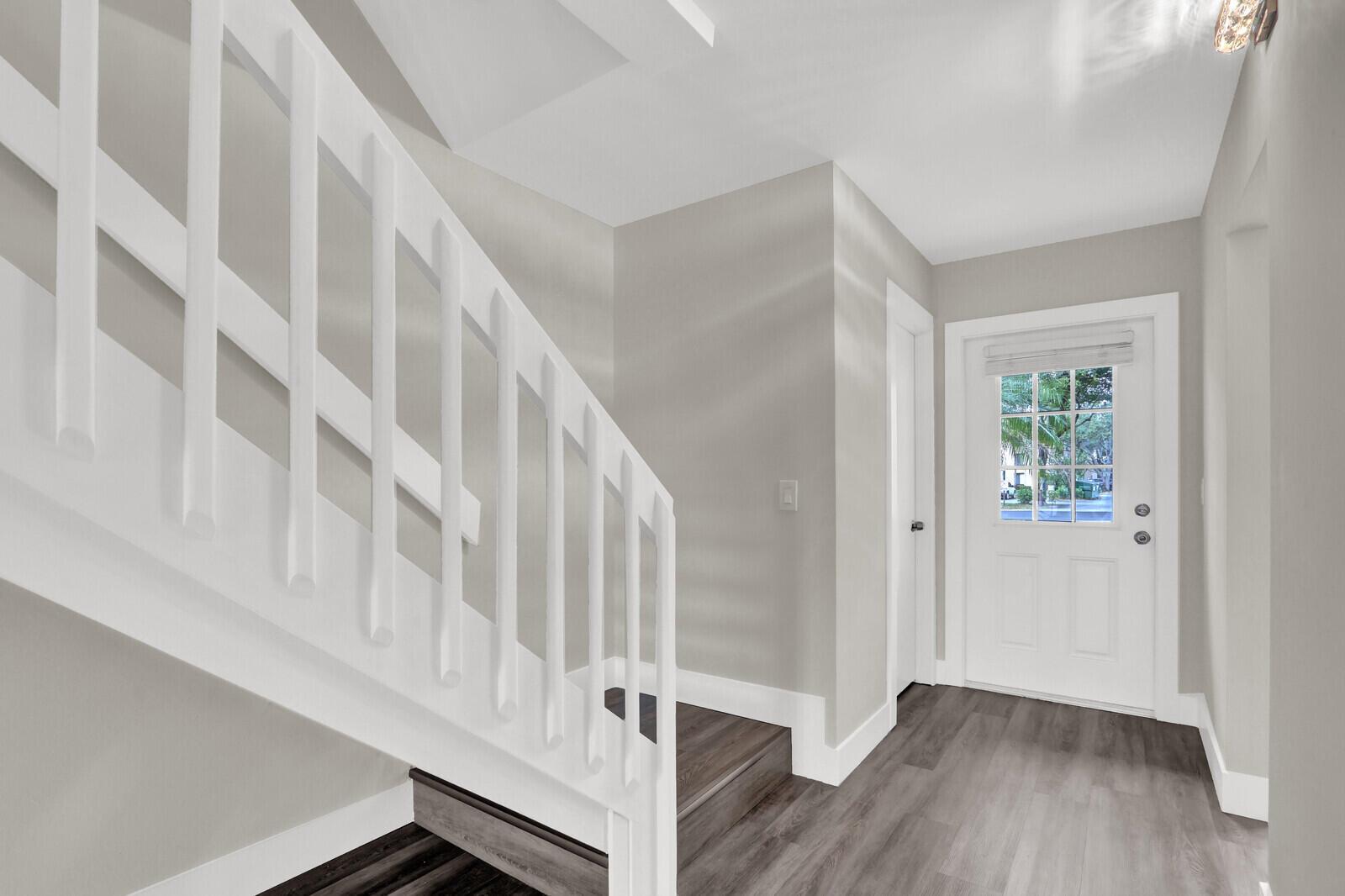 A bright entryway features white stairs, gray wood-look flooring, and a white front door — 234 Foxtail Drive, FL 33415, FL