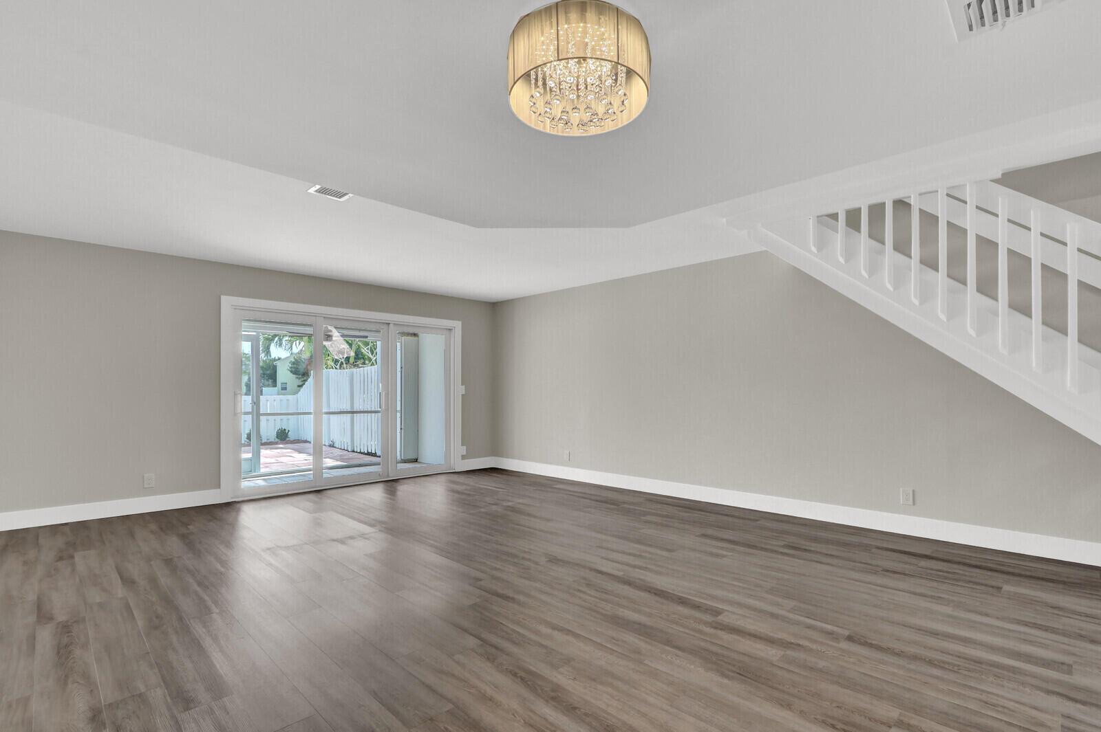 An empty living room features gray wood-look flooring, a crystal chandelier, and a white staircase — 234 Foxtail Drive, FL 33415, FL