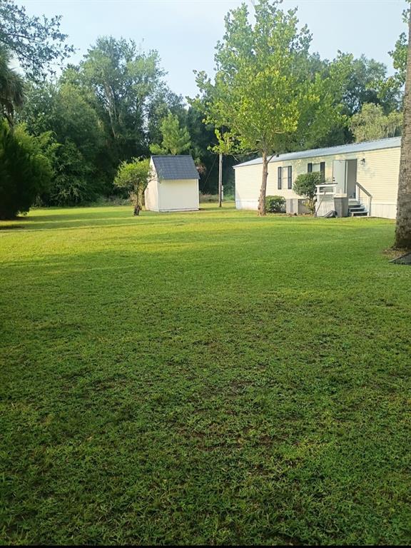 A large grassy backyard features a small storage shed and a mobile home exterior — 105 CANARY LANE, SATSUMA, FL