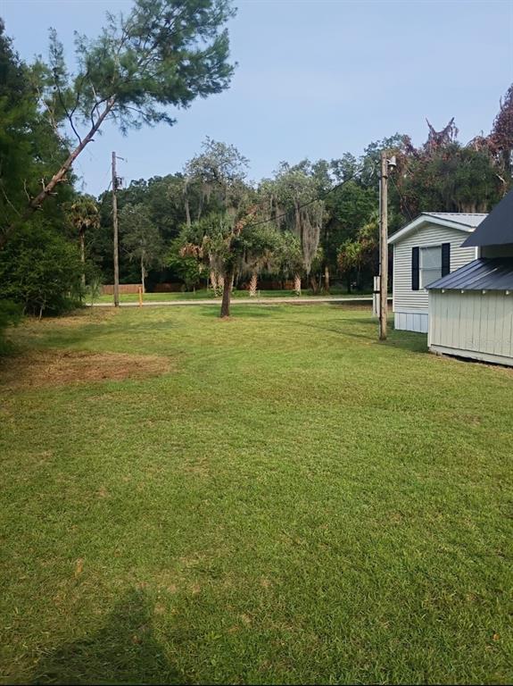 A grassy backyard features a mobile home, utility poles, and mature trees under a clear sky — 105 CANARY LANE, SATSUMA, FL
