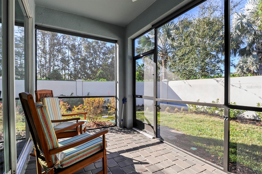A screened-in patio with paver flooring, two wooden chairs, and a view of the backyard — 810 RUDDY QUAIL PLACE, SUN CITY CENTER, FL