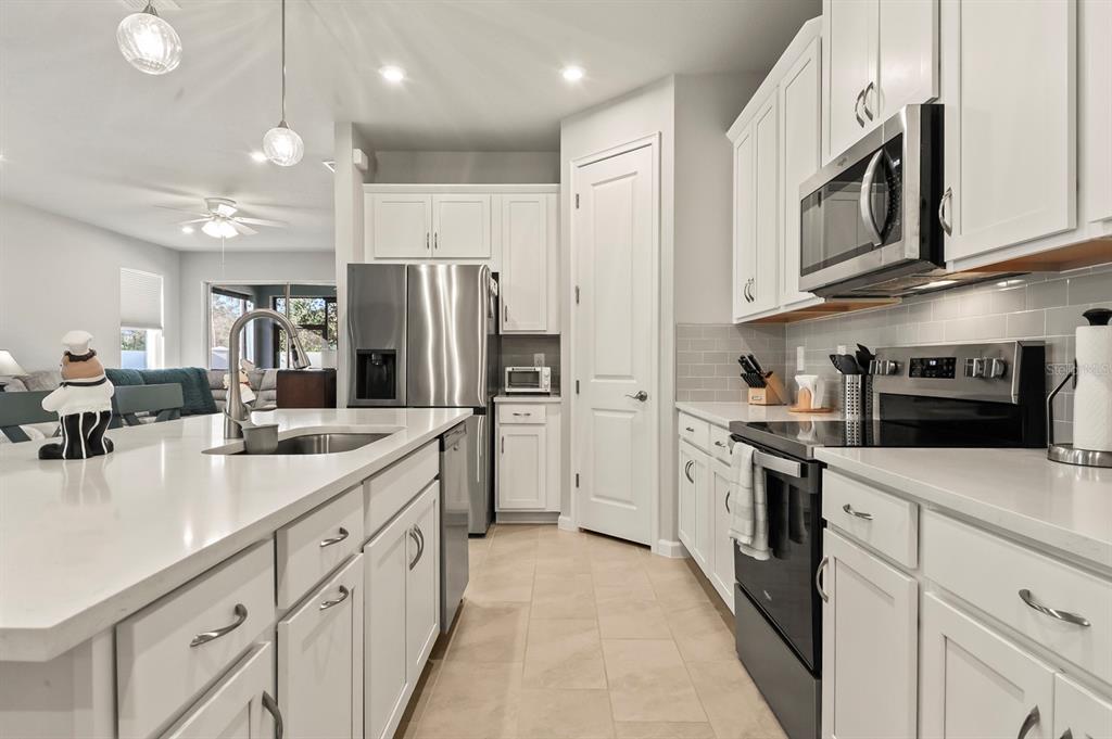 A modern kitchen features white cabinets, stainless steel appliances, a quartz island, and tile flooring — 810 RUDDY QUAIL PLACE, SUN CITY CENTER, FL
