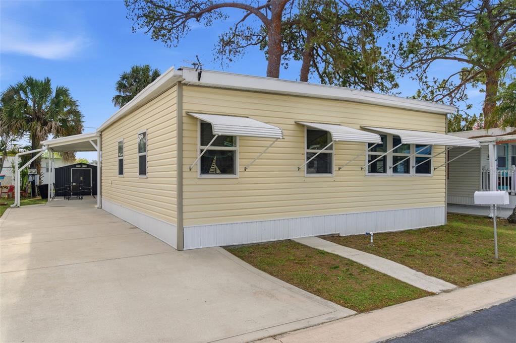 A light yellow mobile home with a concrete driveway and metal window awnings — 7803 46TH AVENUE N UNIT 90, ST PETERSBURG, FL