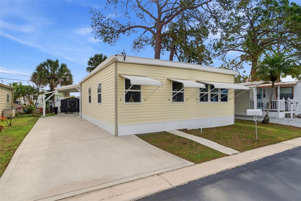 A light yellow mobile home with a concrete driveway and metal window awnings — 7803 46TH AVENUE N UNIT 90, ST PETERSBURG, FL