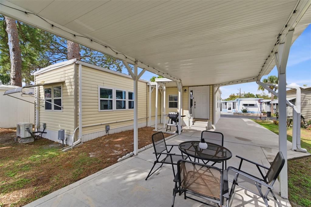 A light yellow mobile home with a covered concrete patio and outdoor seating area — 7803 46TH AVENUE N UNIT 90, ST PETERSBURG, FL