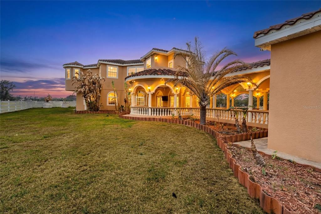 A large, multi-story, orange-stucco house sits behind a white fence in a grassy field — 4015 INDIGO ROAD, GROVELAND, FL