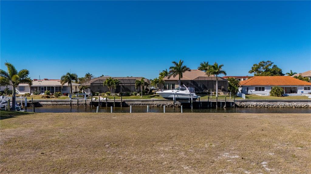 A vacant grassy lot overlooks a canal with houses and a boat on a lift — 7 TROPICANA DRIVE, PUNTA GORDA, FL