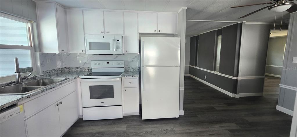 A kitchen with white cabinets, white appliances, and granite-look countertops next to a living area — 10803 FREEDOM DRIVE, PORT RICHEY, FL