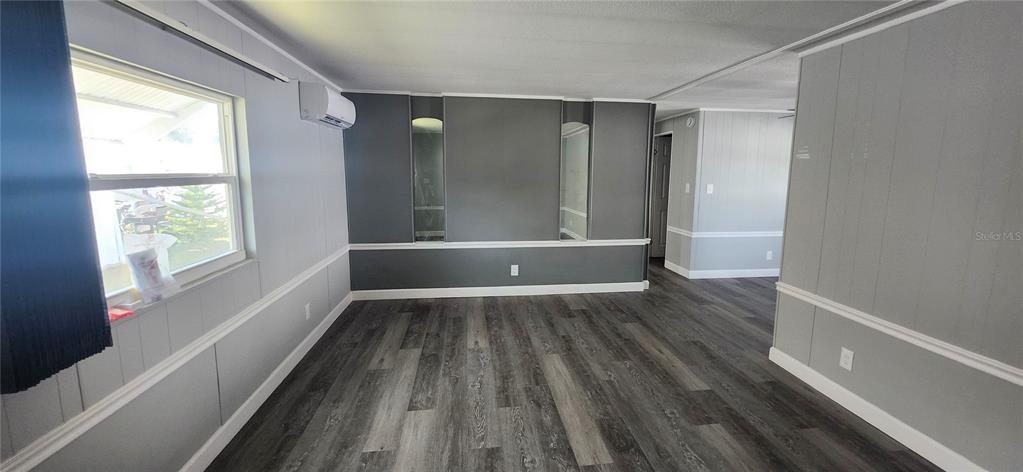 A living room features gray paneled walls, dark wood-look flooring, and a mini-split air conditioner — 10803 FREEDOM DRIVE, PORT RICHEY, FL