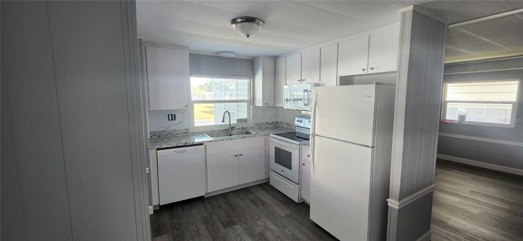 A kitchen features white cabinets, granite-look countertops, stainless steel appliances, and wood-look flooring — 10803 FREEDOM DRIVE, PORT RICHEY, FL