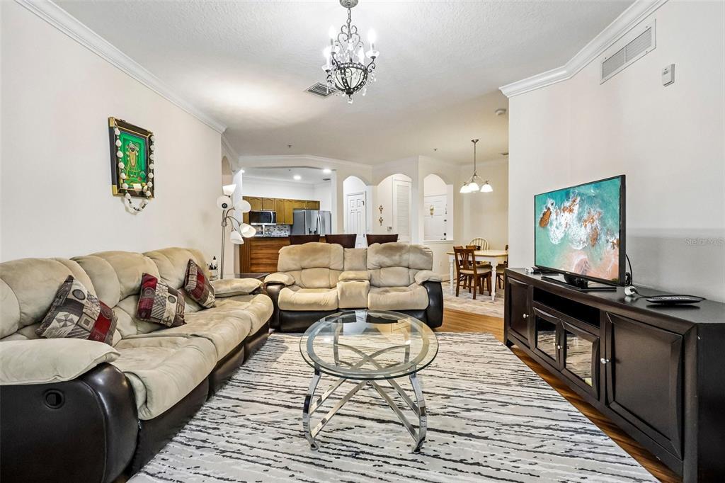 A living room features a beige sofa, a glass coffee table, and a television console — 11446 JASPER KAY TERRACE UNIT 103, WINDERMERE, FL