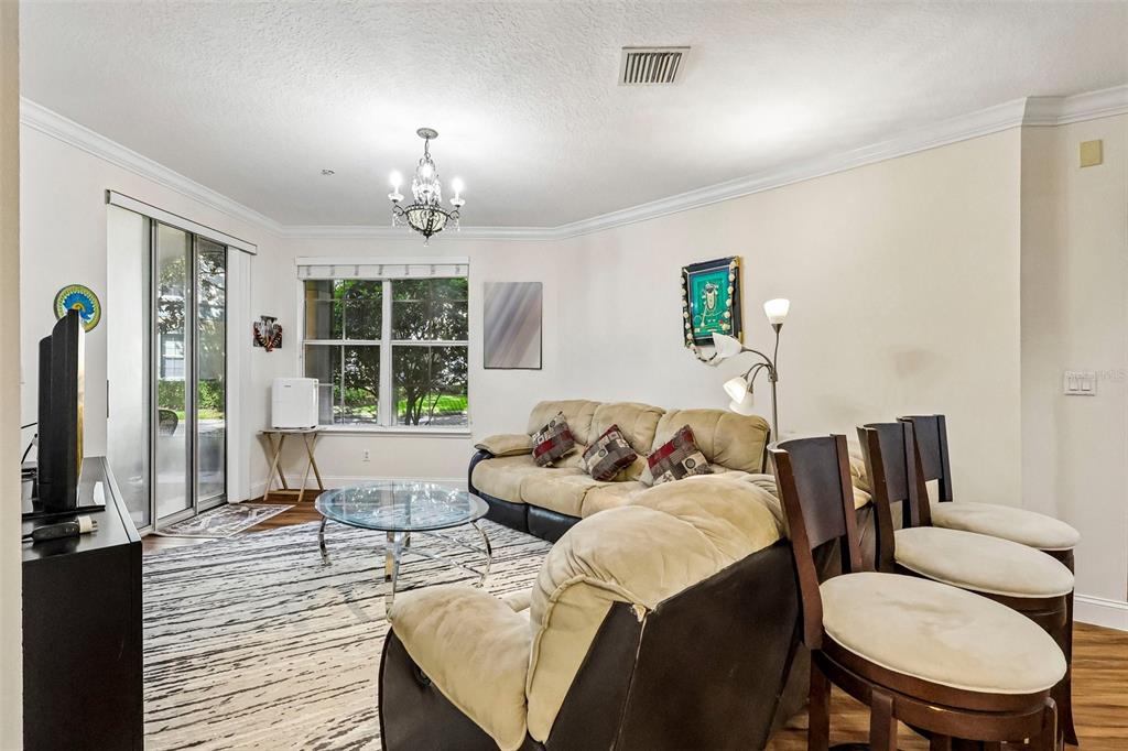 A living room features a beige sofa, glass coffee table, and a chandelier near sliding doors — 11446 JASPER KAY TERRACE UNIT 103, WINDERMERE, FL