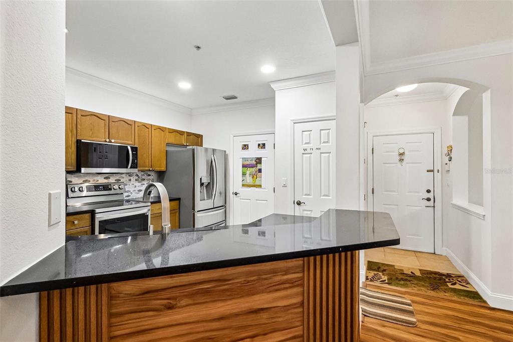 A kitchen with wood cabinets, stainless steel appliances, and a black countertop breakfast bar — 11446 JASPER KAY TERRACE UNIT 103, WINDERMERE, FL
