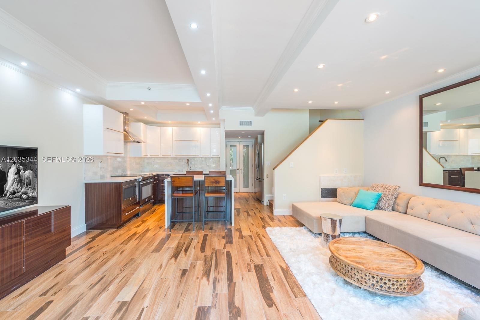 This open-concept living room and kitchen features hardwood flooring, a sectional sofa, and cabinetry — 400 S Pointe Dr # 307, Miami Beach FL 33139, MIAMI BEACH, FL