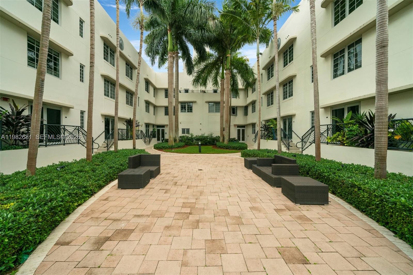 A paved courtyard features palm trees, dark outdoor furniture, and surrounding multi-story residential buildings — 435 21st St # 103, Miami Beach FL 33139, MIAMI BEACH, FL