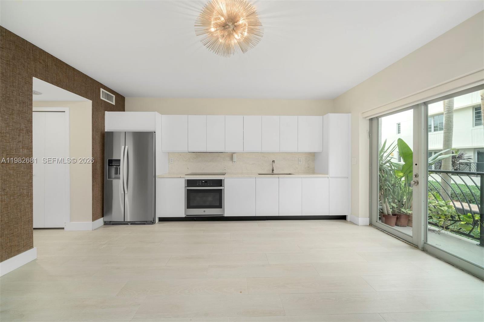 A modern kitchen features white cabinetry, stainless steel appliances, and a glass door to a balcony — 435 21st St # 103, Miami Beach FL 33139, MIAMI BEACH, FL