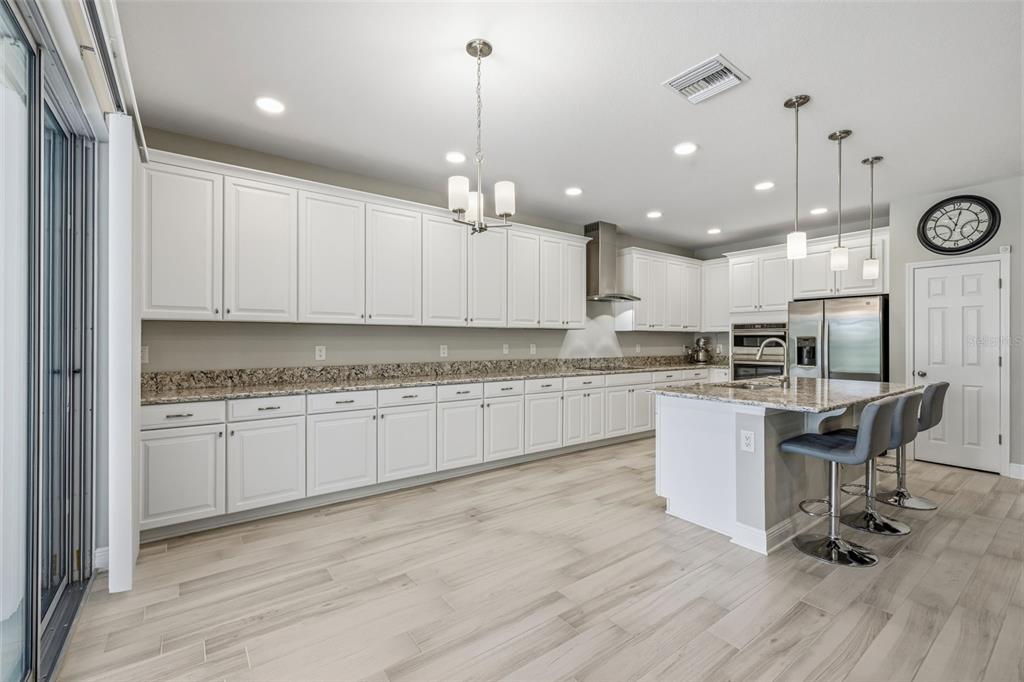 A modern kitchen features white cabinetry, granite countertops, a center island, and light wood flooring — 12000 NOUVEAU AVENUE, SPRING HILL, FL