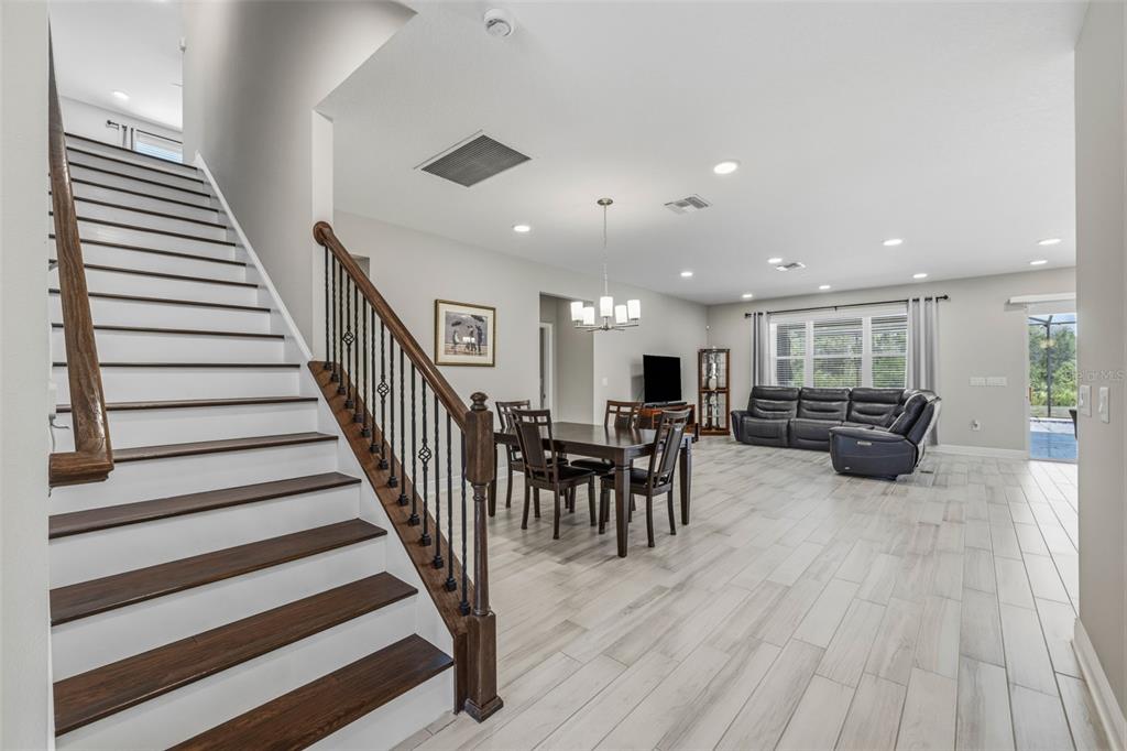 An open-concept living and dining area features wood-look tile flooring and a staircase with railings — 12000 NOUVEAU AVENUE, SPRING HILL, FL