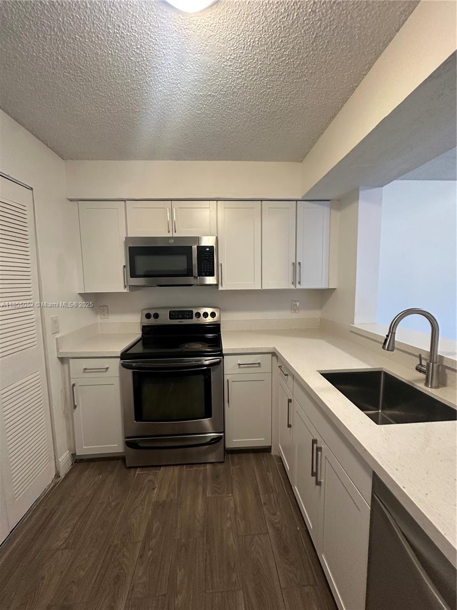 A kitchen features white cabinets, stainless steel appliances, and light-colored countertops over wood-look flooring — 1245 SW 46th Ave # 1202, Pompano Beach FL 33069, POMPANO BEACH, FL