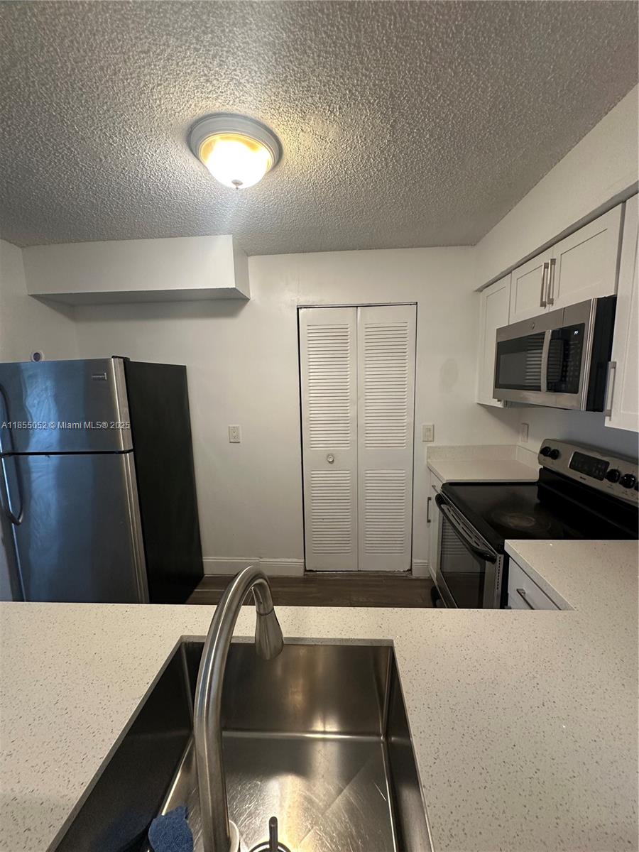 A kitchen features stainless steel appliances, white cabinets, a quartz countertop, and a double-door closet — 1245 SW 46th Ave # 1202, Pompano Beach FL 33069, POMPANO BEACH, FL