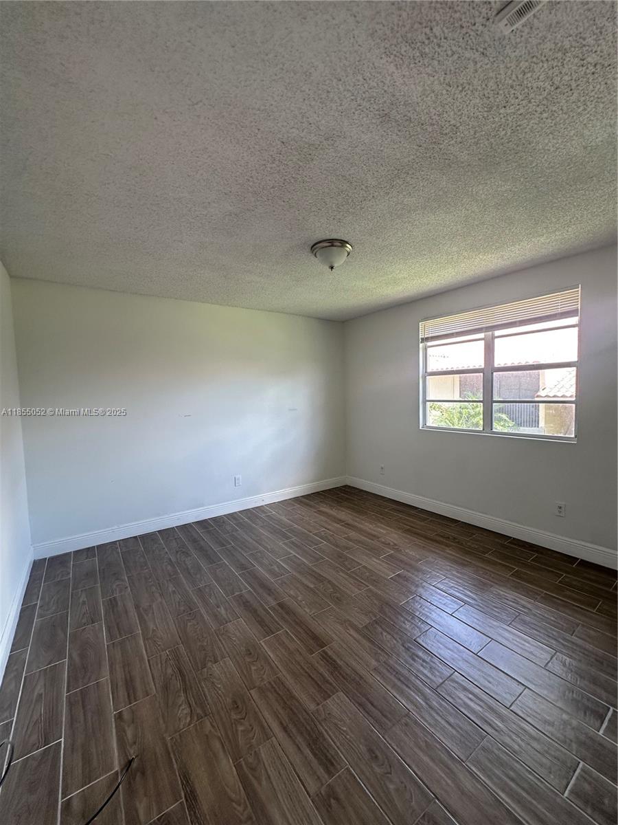 An empty bedroom features wood-look tile flooring, white walls, and a single window — 1245 SW 46th Ave # 1202, Pompano Beach FL 33069, POMPANO BEACH, FL