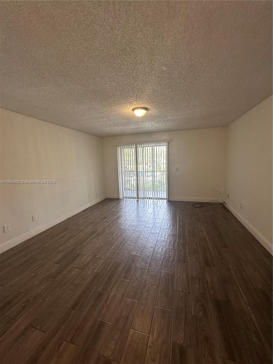 An empty room features wood-look tile flooring, white walls, and a sliding glass door — 1245 SW 46th Ave # 1202, Pompano Beach FL 33069, POMPANO BEACH, FL