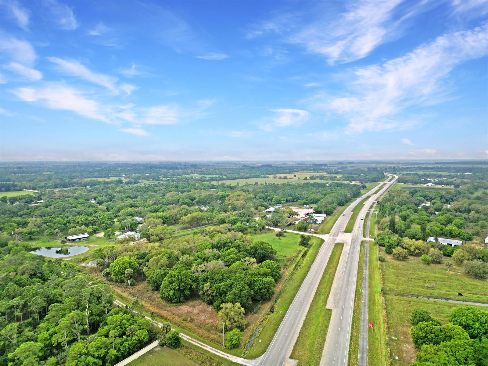 An aerial view shows a divided highway running through a rural, wooded landscape with buildings — 11275 Okeechobee Road, Fort Pierce FL 34945, FORT PIERCE, FL