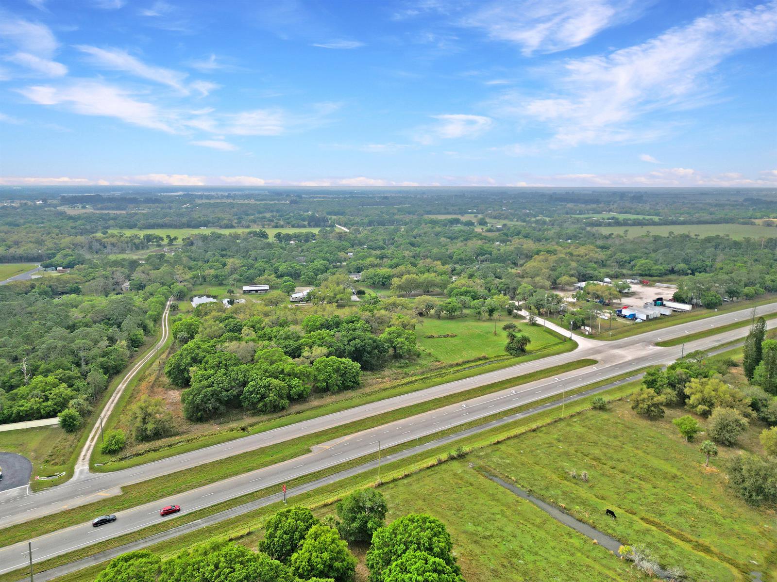 An aerial view shows a multi-lane highway running through a rural, tree-filled landscape — 11275 Okeechobee Road, Fort Pierce FL 34945, FORT PIERCE, FL