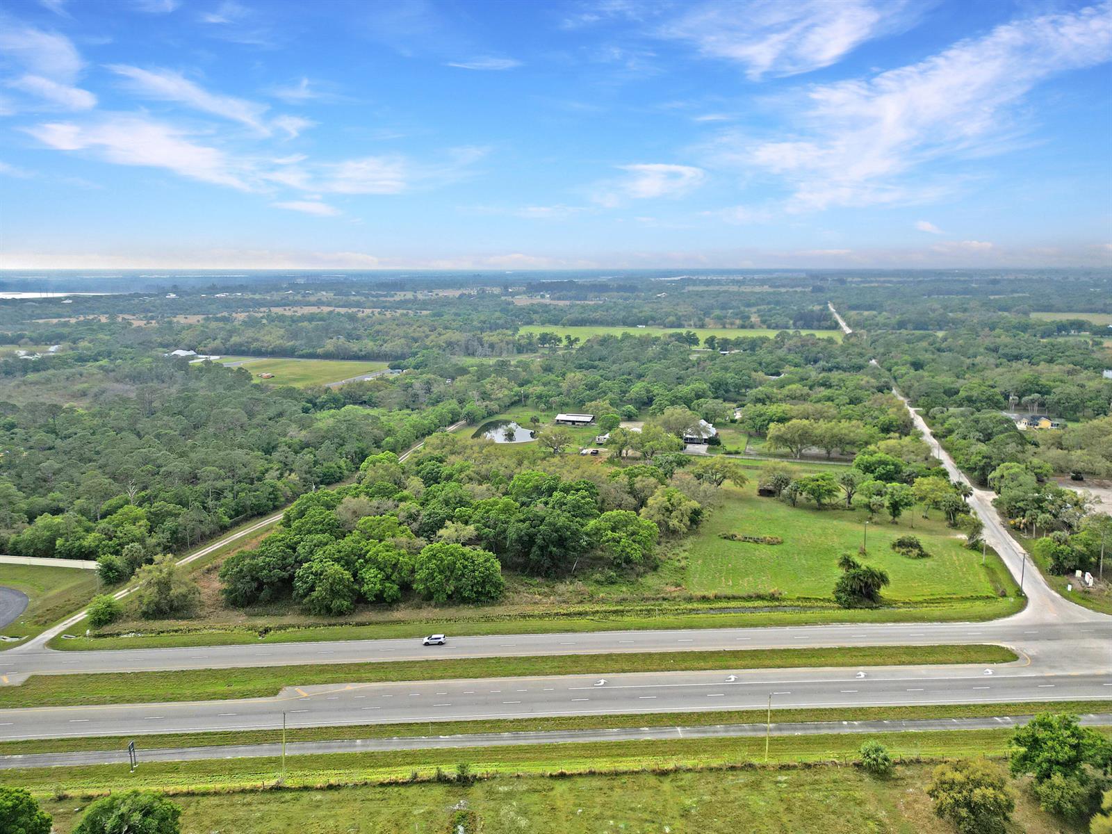 An aerial view shows a rural property with a house, pond, and trees near a highway — 11275 Okeechobee Road, Fort Pierce FL 34945, FORT PIERCE, FL