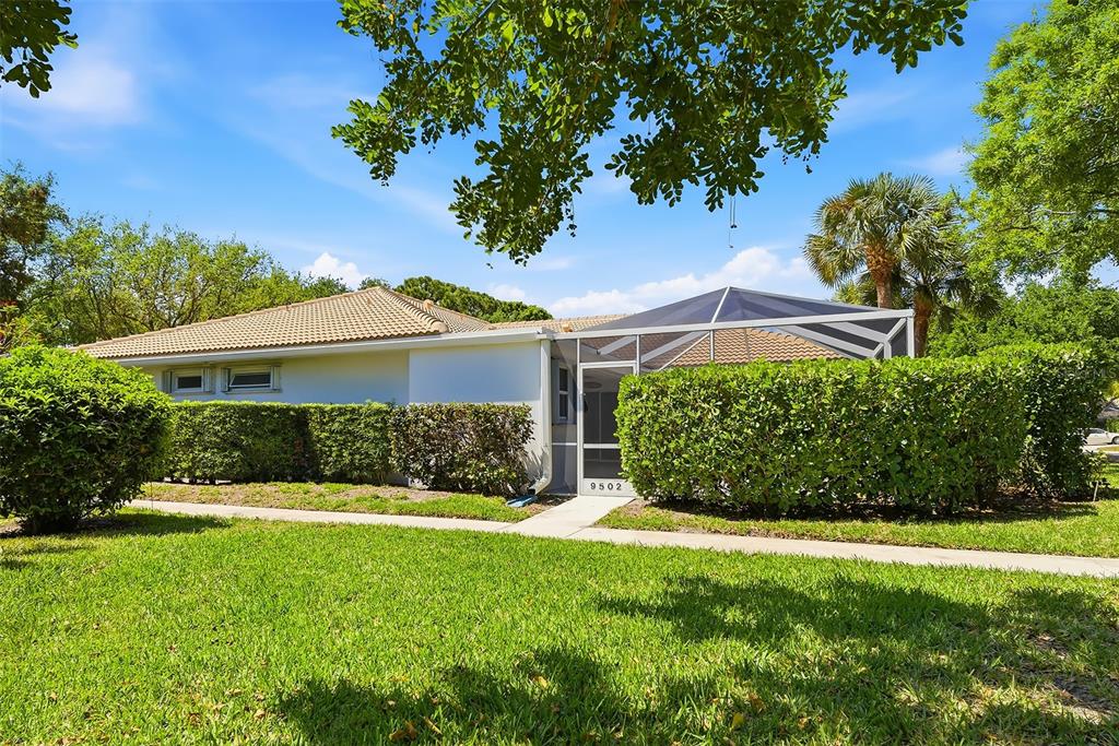 A single-story house with a screened-in patio and a manicured hedge in the front yard — 9502 CHAPMAN OAK COURT, PALM BEACH GARDENS, FL
