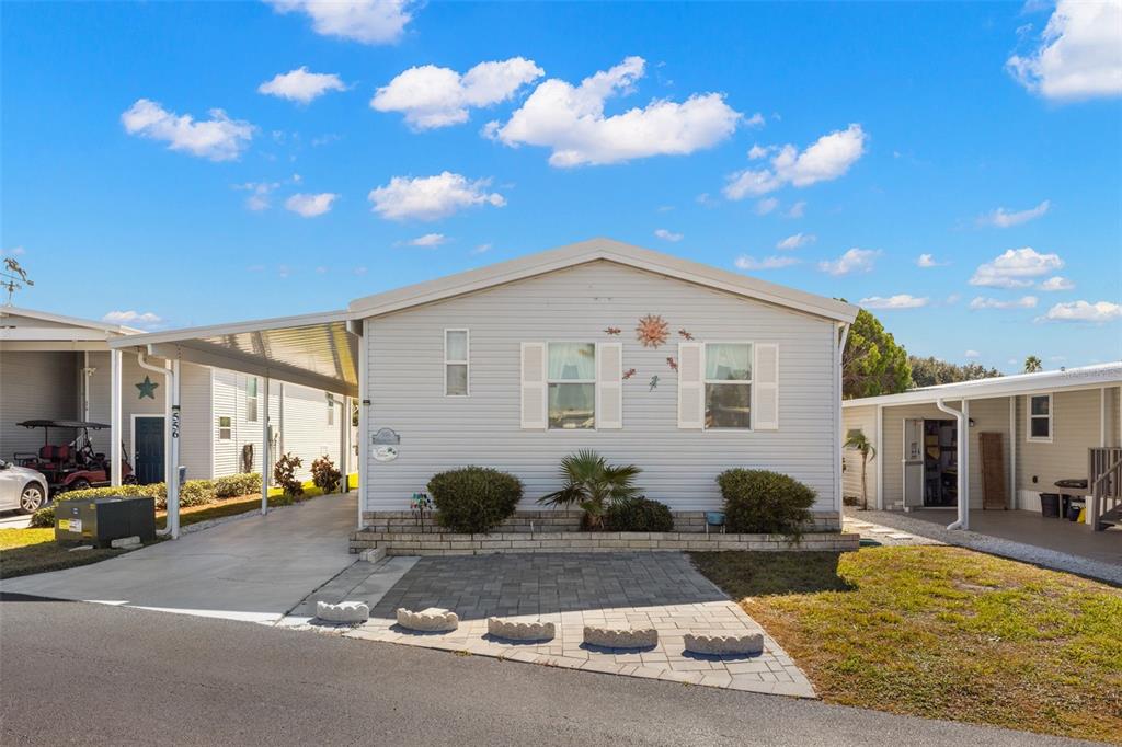 A light-gray manufactured home features a carport, a paver patio, and a small front garden — 556 MOUNT OAK AVENUE NE UNIT 738, ST PETERSBURG, FL