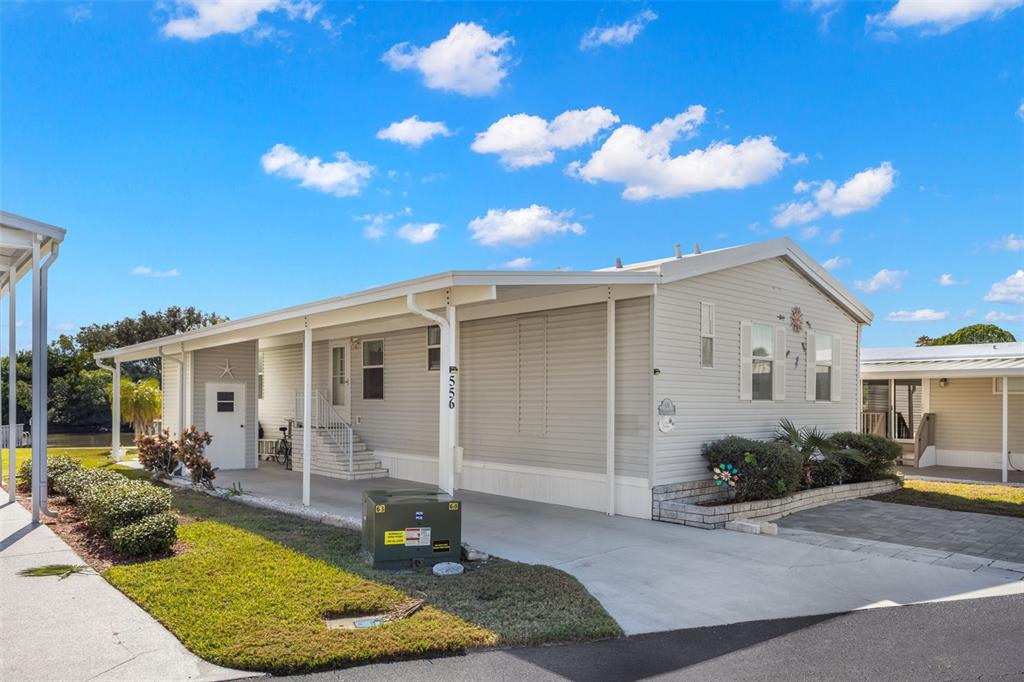 A light-colored manufactured home features a covered carport, a concrete driveway, and a small lawn — 556 MOUNT OAK AVENUE NE UNIT 738, ST PETERSBURG, FL