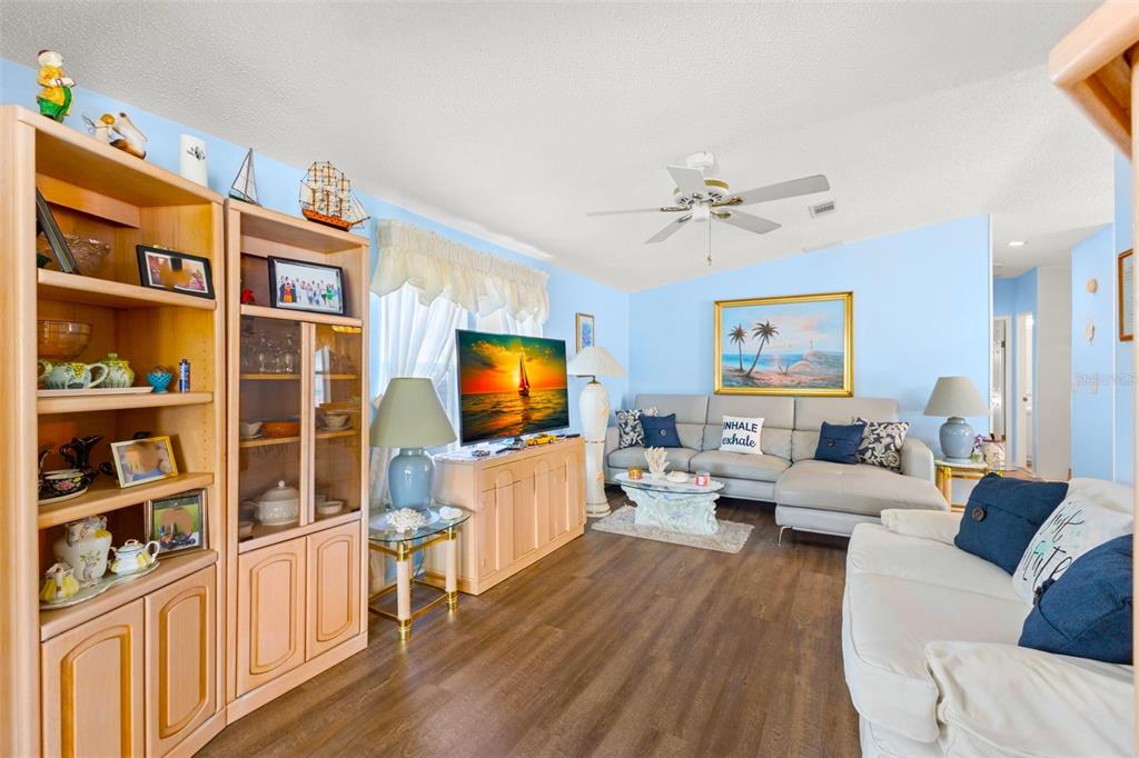 A living room with light blue walls, wood-look flooring, a sectional sofa, and wooden shelving — 556 MOUNT OAK AVENUE NE UNIT 738, ST PETERSBURG, FL