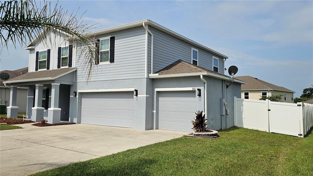 A two-story house with light blue siding, a three-car garage, and a white vinyl fence — 1921 BELL CREEK LOOP, FRUITLAND PARK, FL