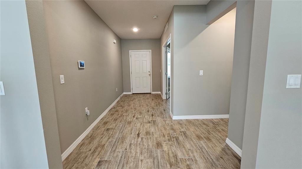 A hallway with wood-look tile flooring leads to a white door — 1921 BELL CREEK LOOP, FRUITLAND PARK, FL