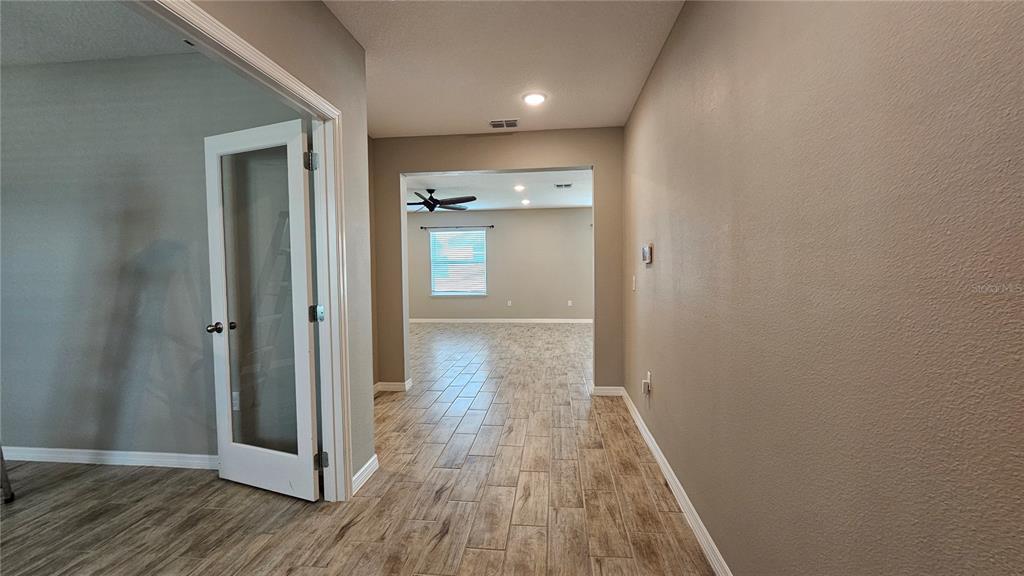 A hallway with wood-look tile flooring leads to an open living area with a window — 1921 BELL CREEK LOOP, FRUITLAND PARK, FL