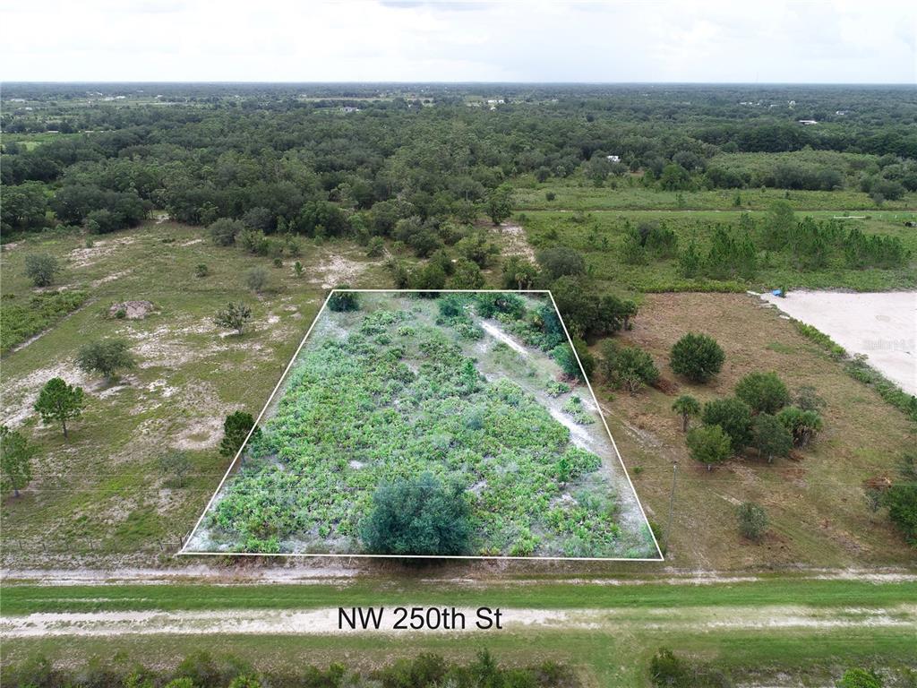 An aerial view shows a rectangular, undeveloped plot of land bordered by a dirt road — 18235 NW 250TH STREET, OKEECHOBEE, FL