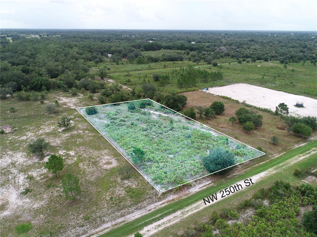 An aerial view shows a rectangular, undeveloped plot of land bordering a dirt road — 18235 NW 250TH STREET, OKEECHOBEE, FL