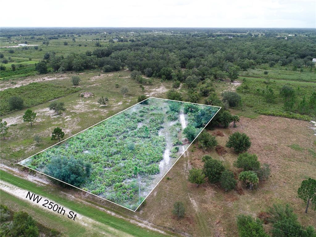 An aerial view shows a rectangular, tree-covered lot bordering a dirt road — 18235 NW 250TH STREET, OKEECHOBEE, FL
