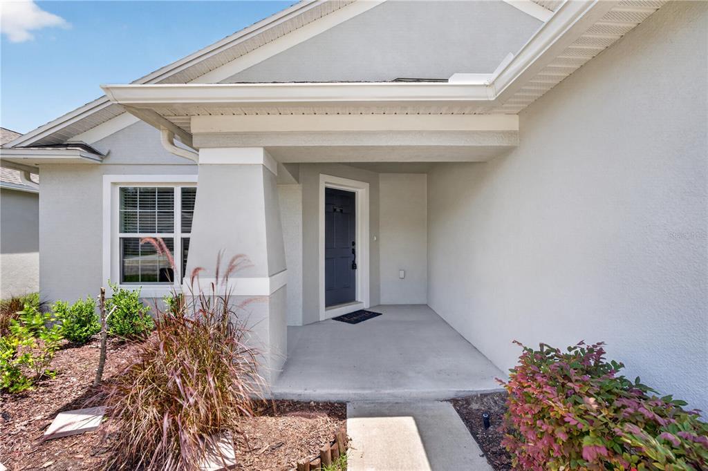 A covered concrete porch leads to a dark blue front door of a suburban home — 1919 THOMPSON PRESERVE BOULEVARD, BARTOW, FL