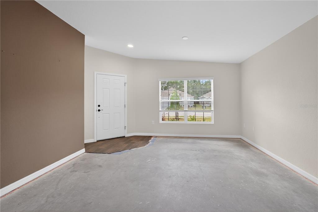 An unfinished room features a white front door, a large window, and exposed concrete flooring — 1919 THOMPSON PRESERVE BOULEVARD, BARTOW, FL